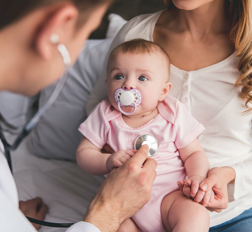 a baby sitting in their mother's lap whilst being examined with a stethoscope