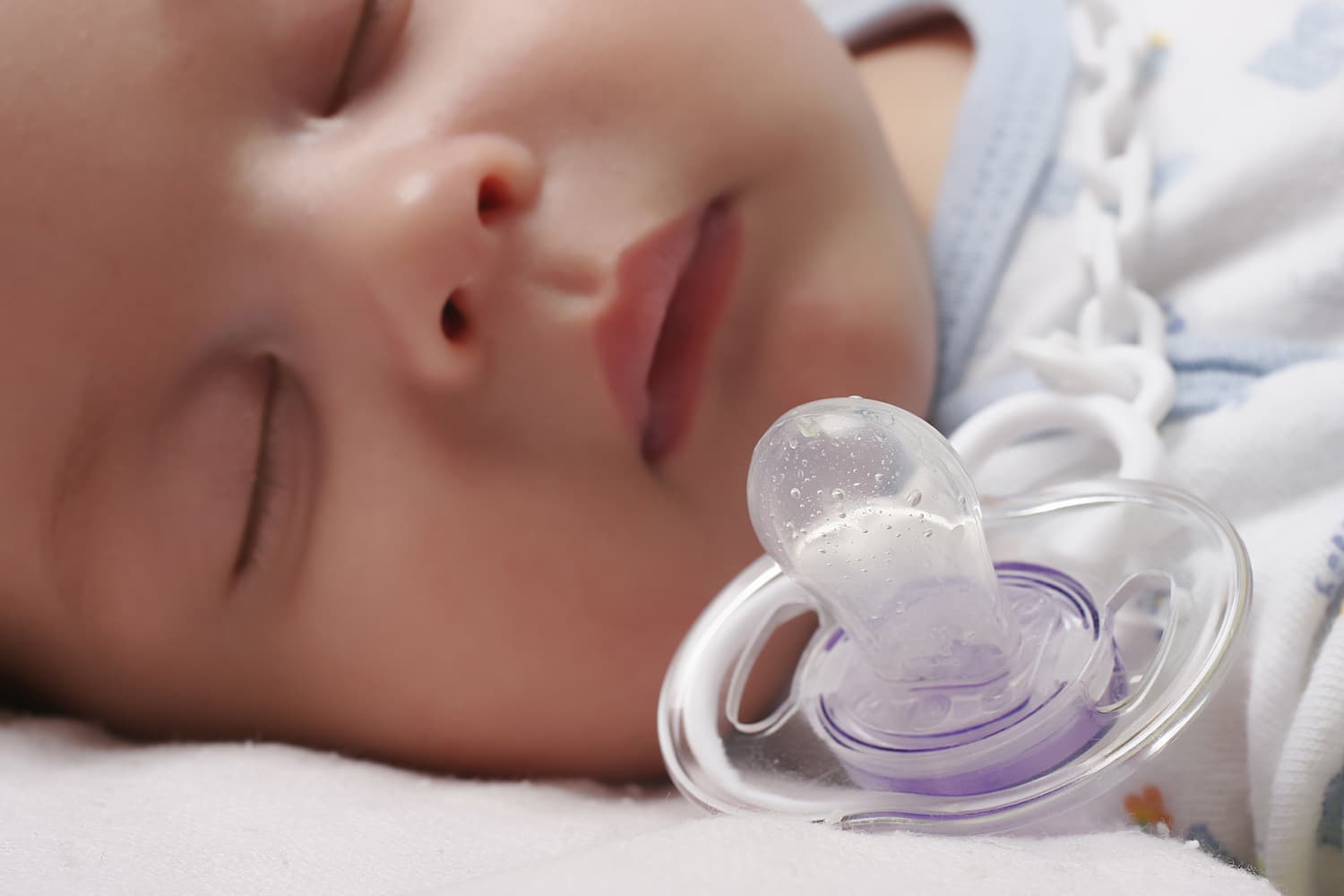 A close up of a baby sleeping next to their dummy