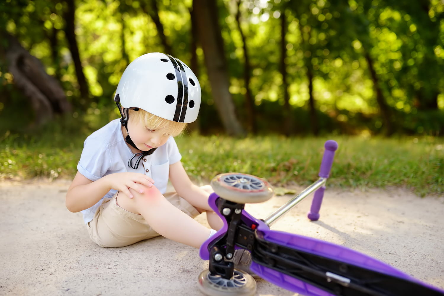A child holding his knee because he just fell off his scooter