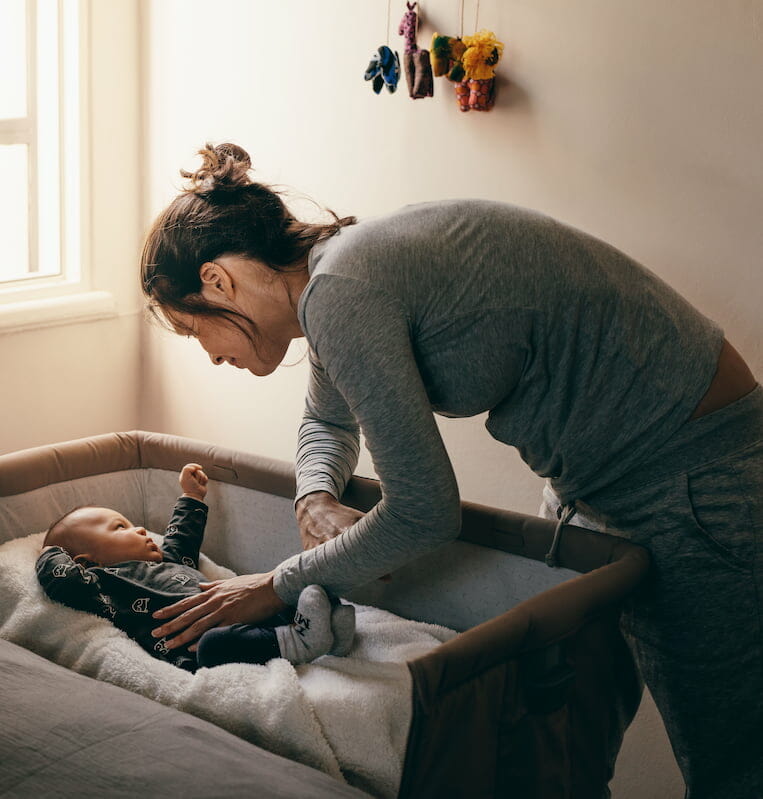 A mother comforting their baby in their cot