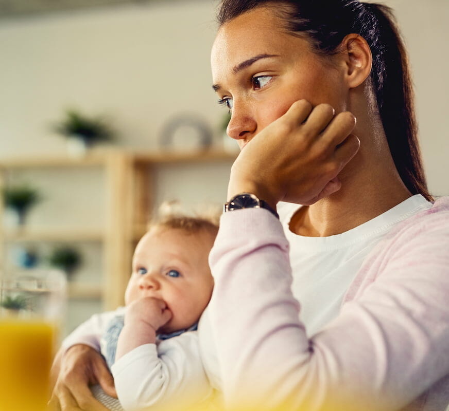 a mother holding her baby whilst resting her head in her hand