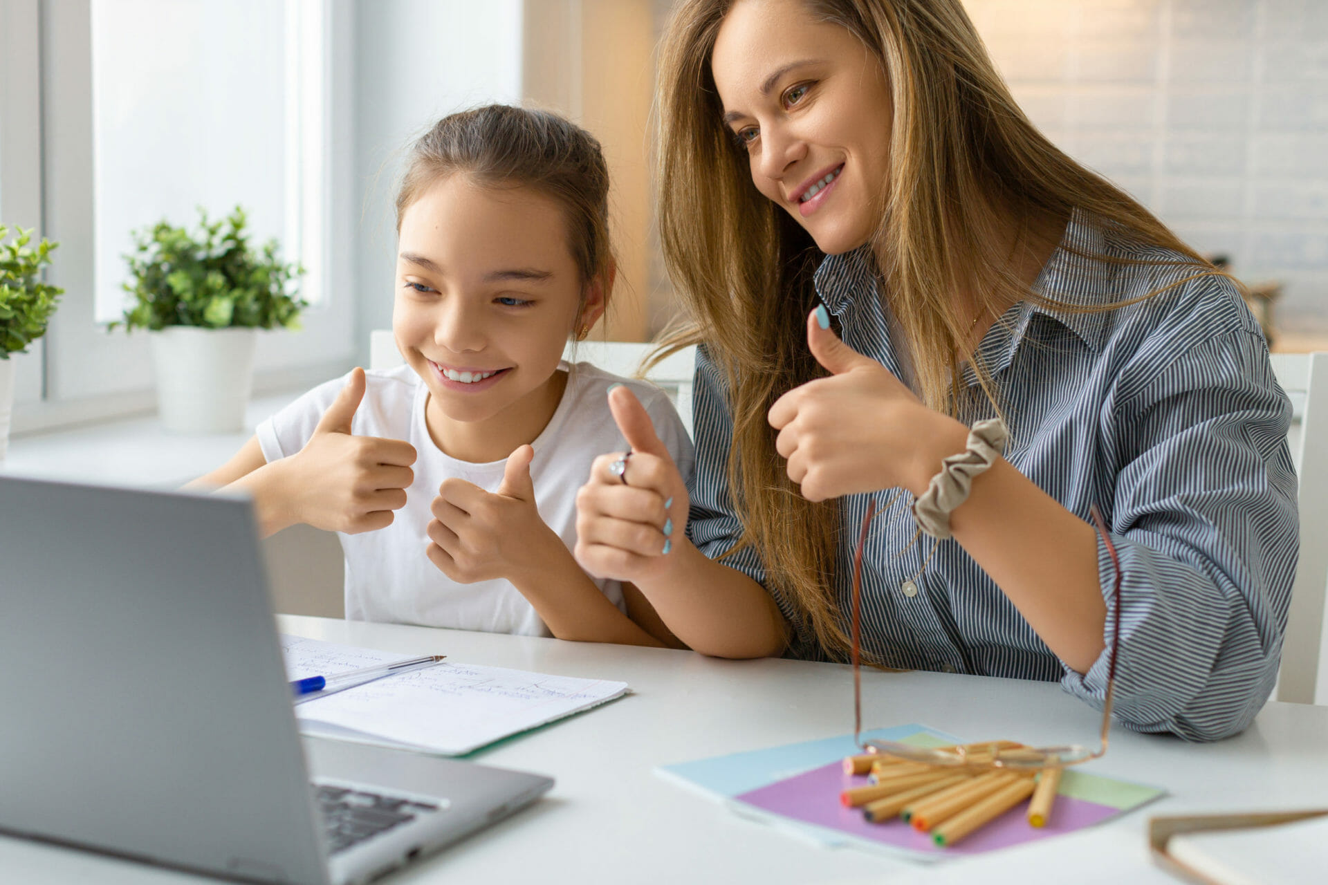A teenage girl and her mother are holding their thumbs up to a laptop screen