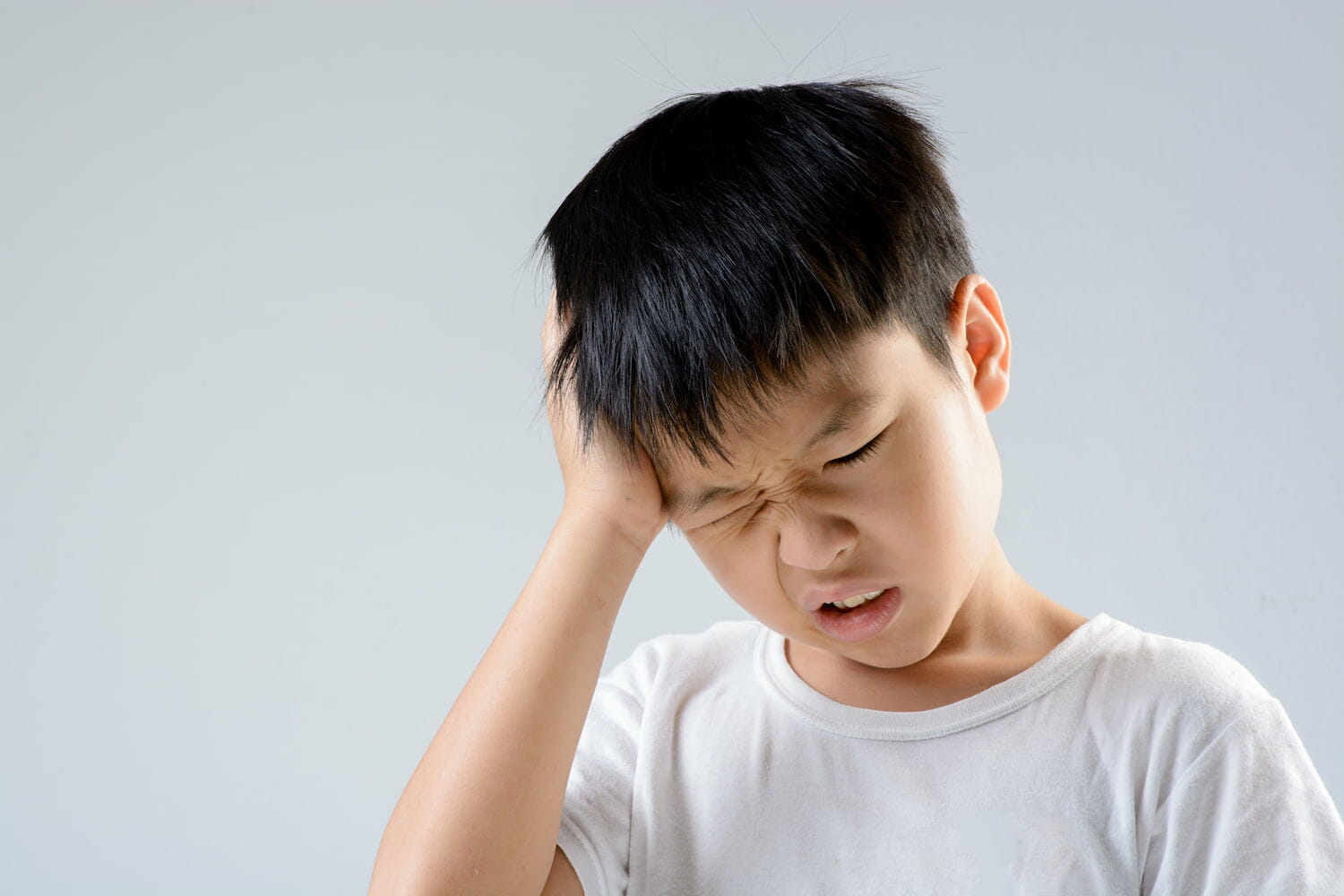 A child holding their head and wincing in pain