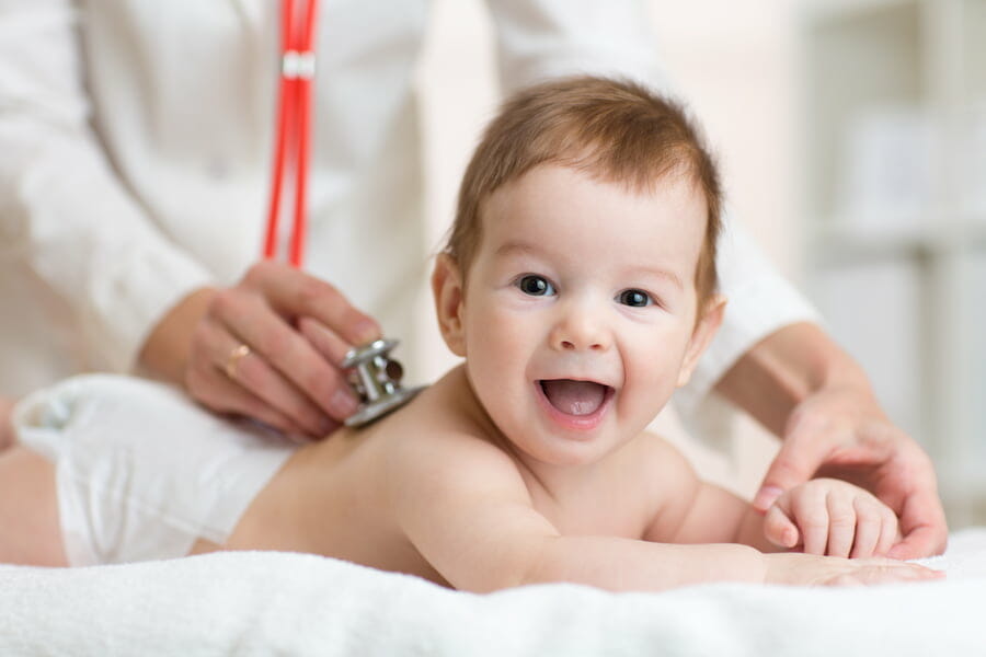 a baby lying on their front whilst being examined with a stethoscope