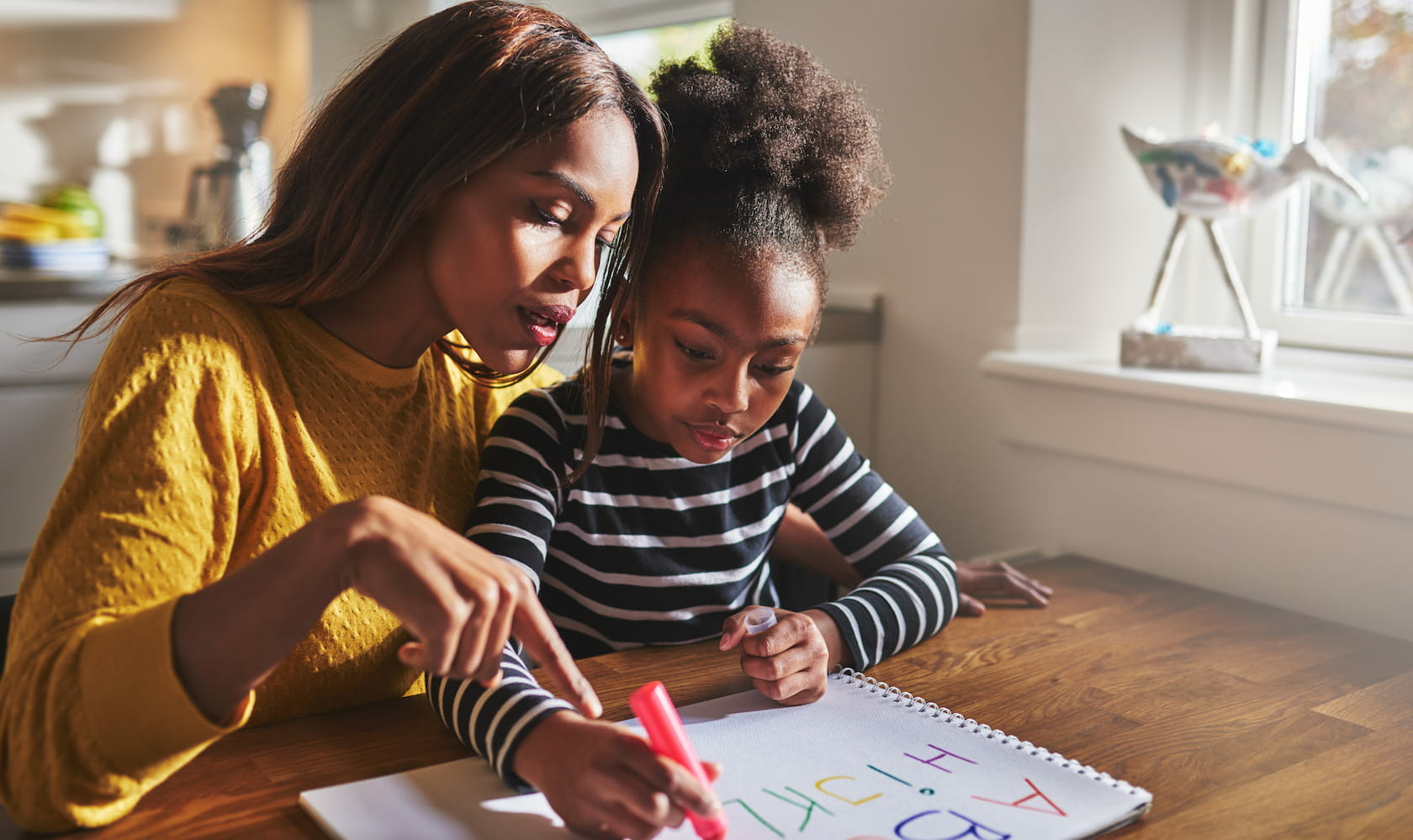 a mother and child sat at a table drawing out letters