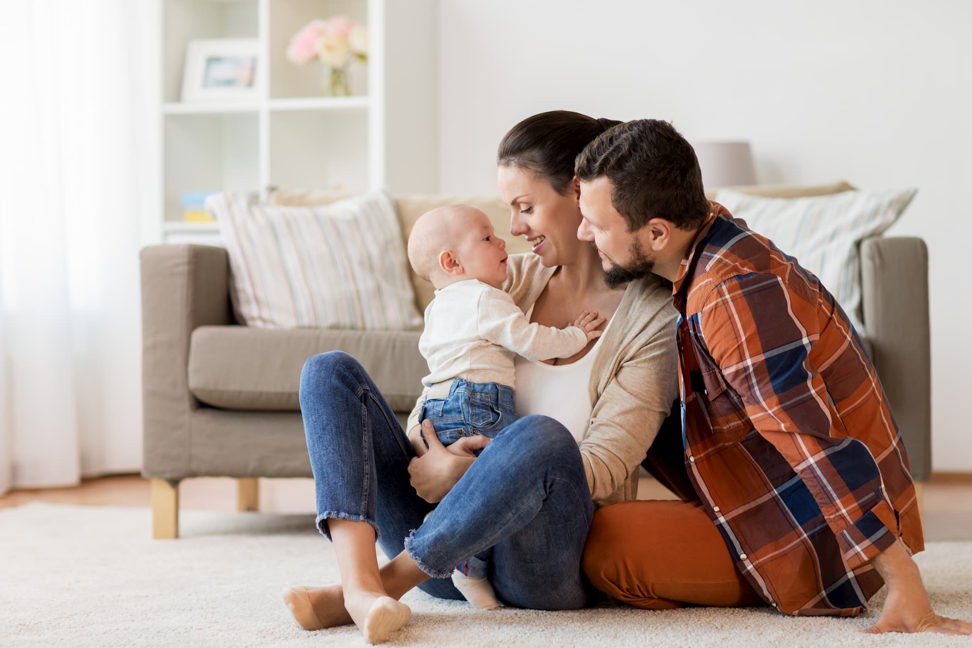 Parents cuddling their baby whilst sat on the floor in their living room