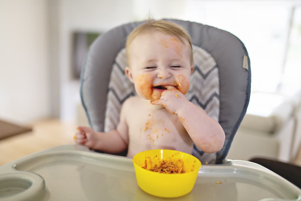 a child eating in their high chair and laughing