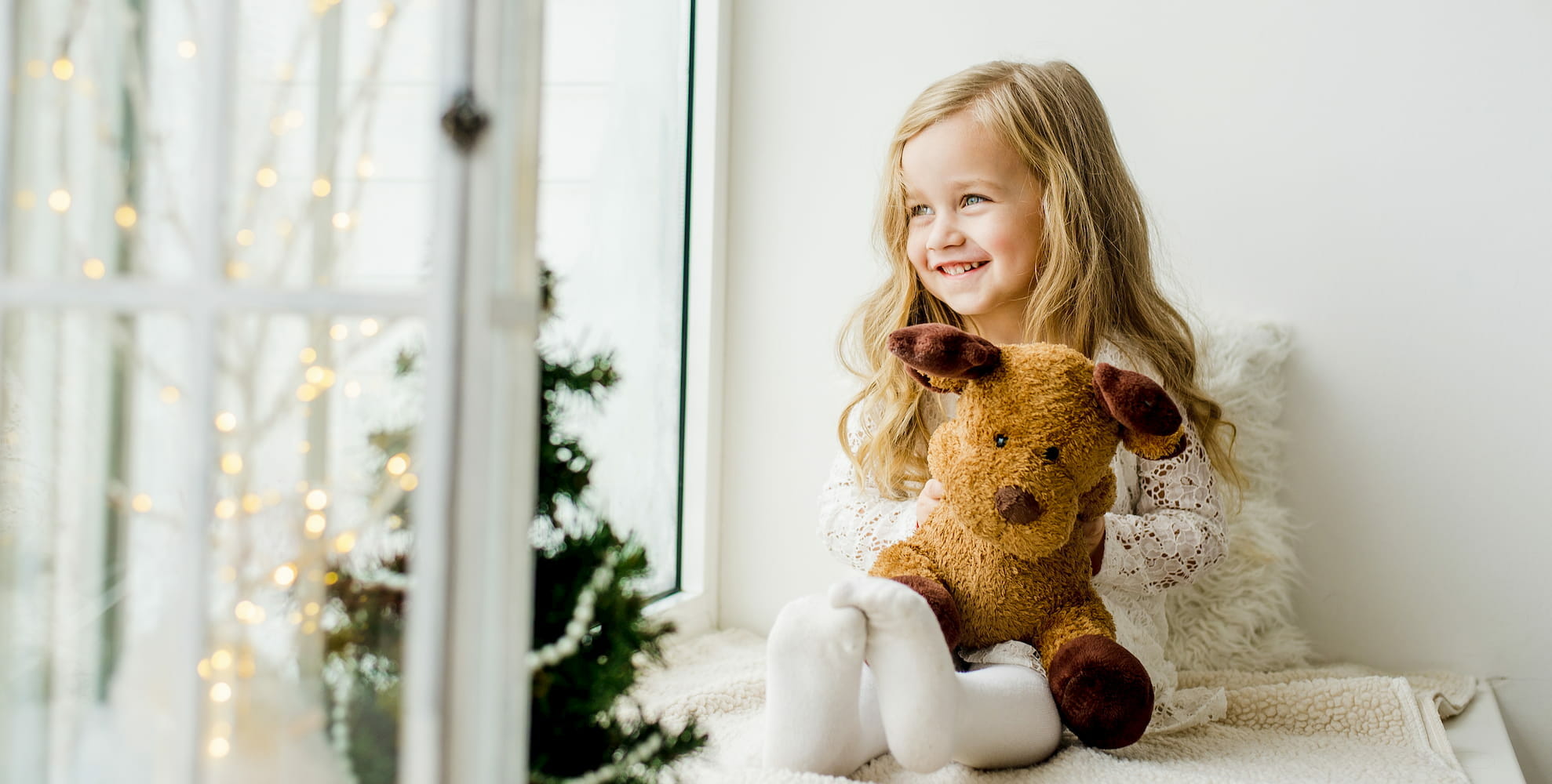 a child smiling whilst looking out the window and holding her stuffed animal