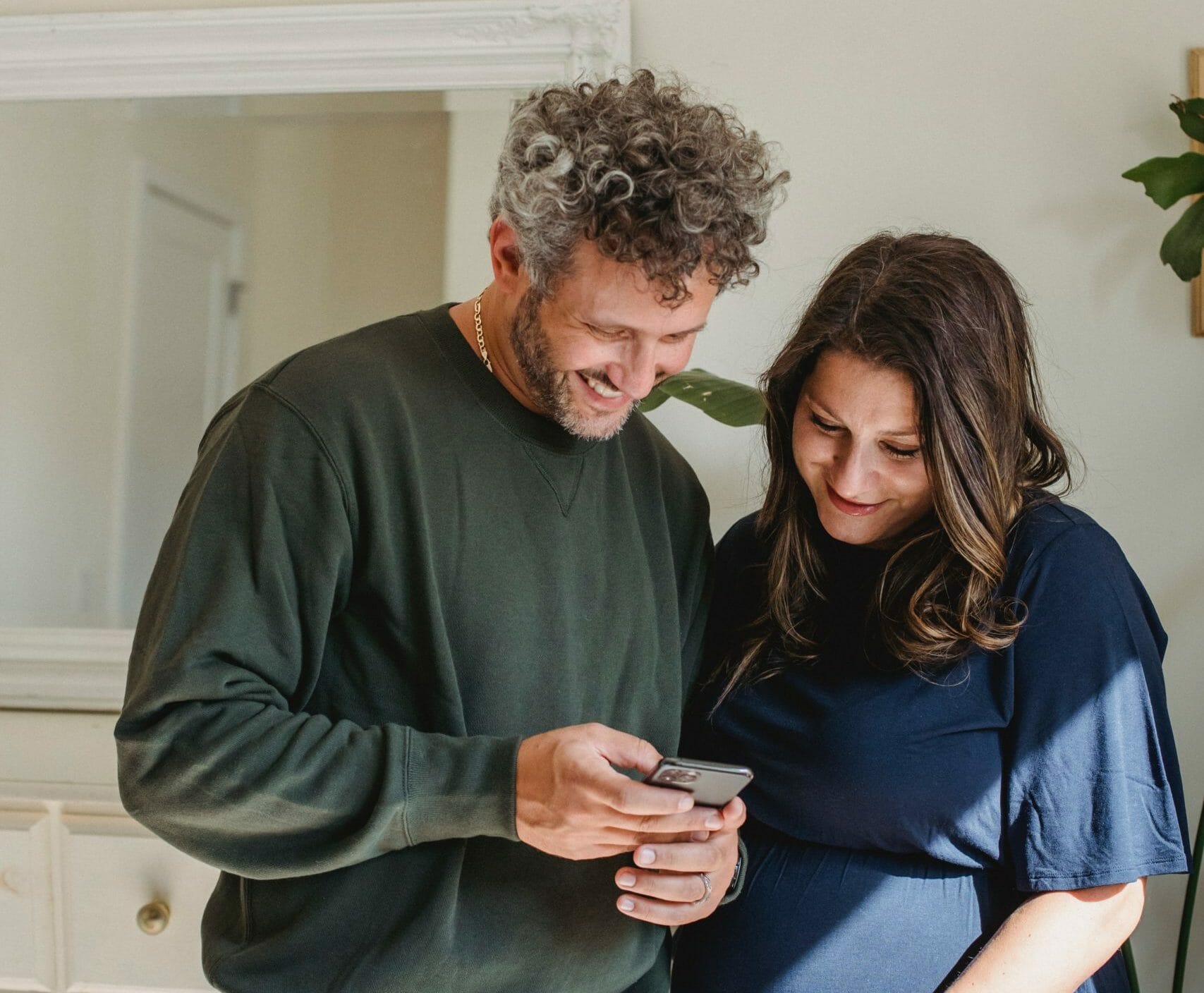 A couple laughing whilst looking down at a phone