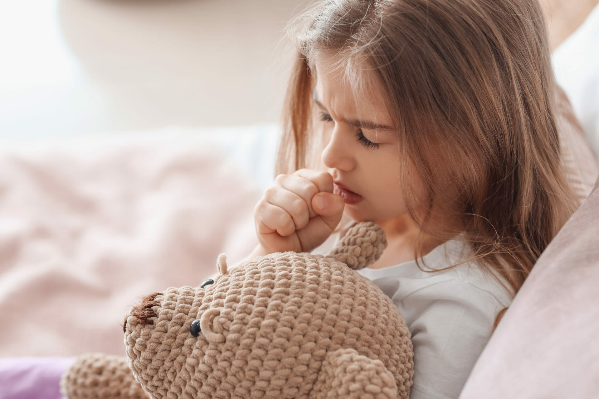 Sick girl at home cuddling her toy bear